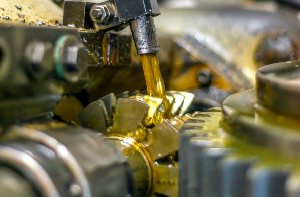 Close-up of interlocking gears being lubricated by a stream of golden oil, showing the intricate details and shiny metal surfaces of the mechanical components.
