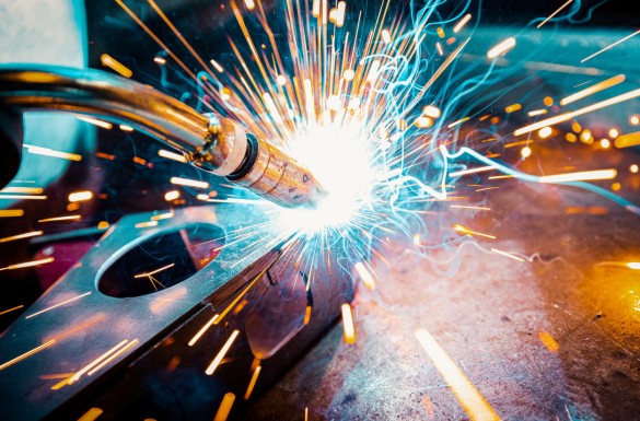 A close-up of a welding process with bright sparks flying outward, creating an intense burst of light. The welding torch is in contact with metal pieces, surrounded by vibrant orange and blue sparks.