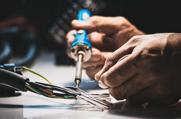 A person using a soldering iron to connect multiple wires on a white surface, with a focus on the hands and the tool.